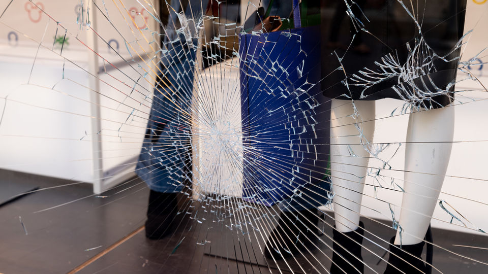 legs of dressed male and female mannequins in retail store with broken plate glass window
