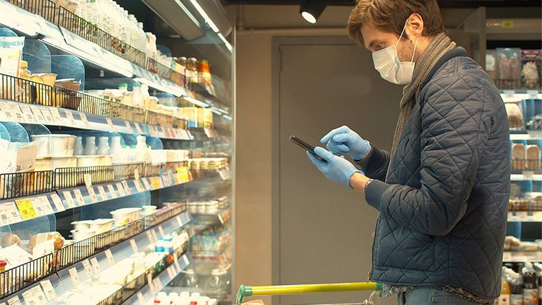 male shopper wearing mask and gloves using device at retail shelves