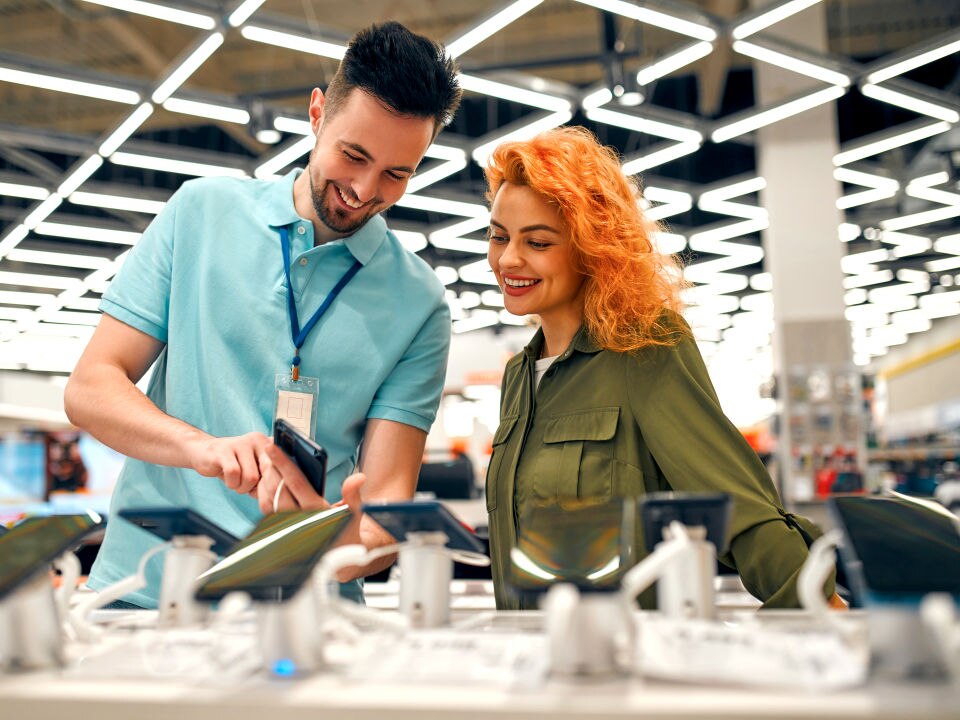 male retail electronics department employee helping female shopper select a phone