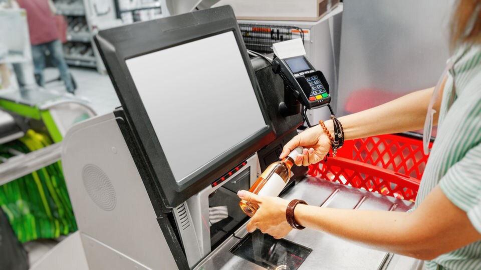 woman scanning bottle of wine at retail self-checkout station