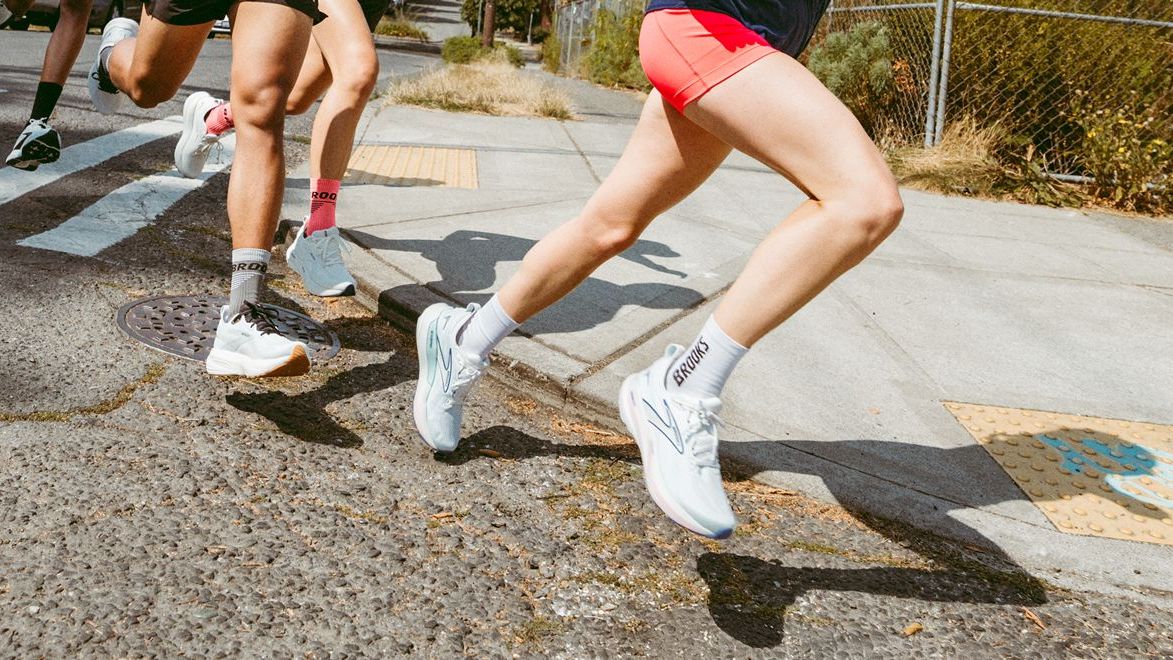 closeup on legs of several runners wearing brooks running branded shoes and socks running next to the sidewalk in a suburban area