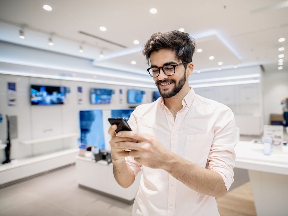 smiling male shopper choosing a new cellphone in a retail electronics store