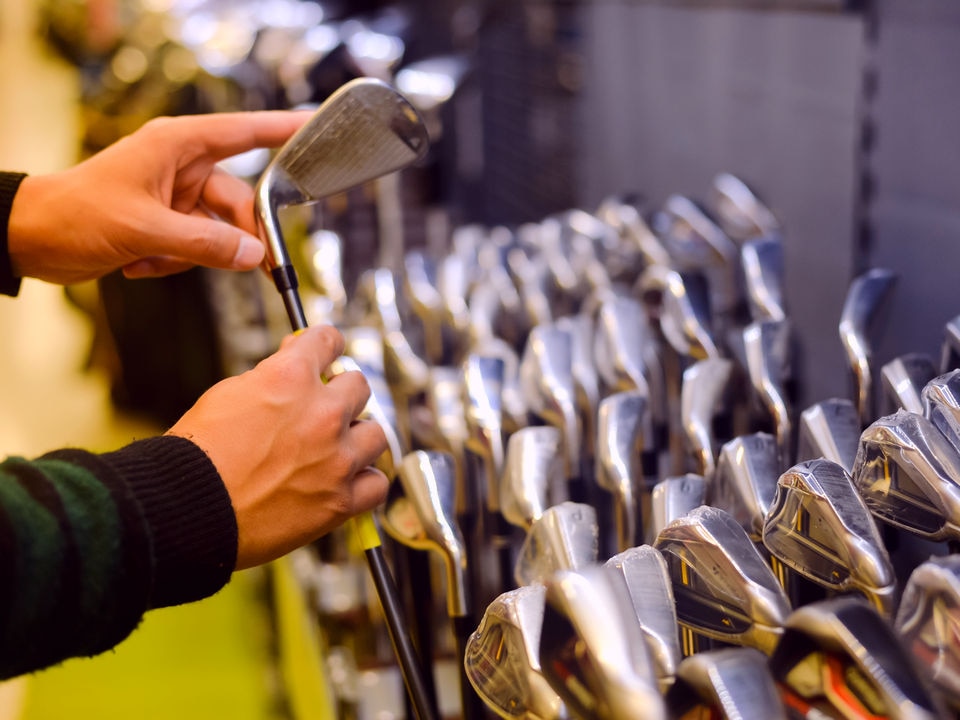 male customer handling golf clubs in retail sporting goods store