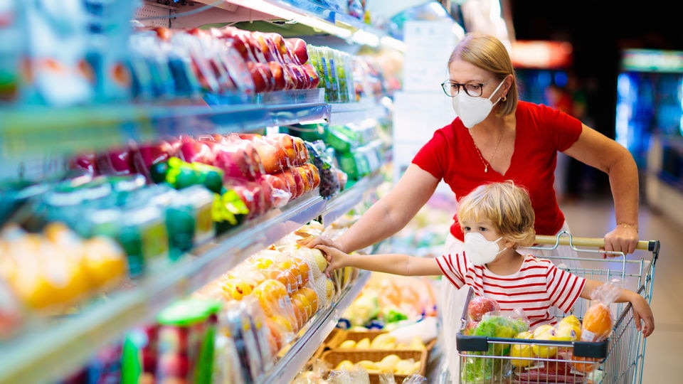 masked woman pushes masked child in shopping cart through retail supermarket