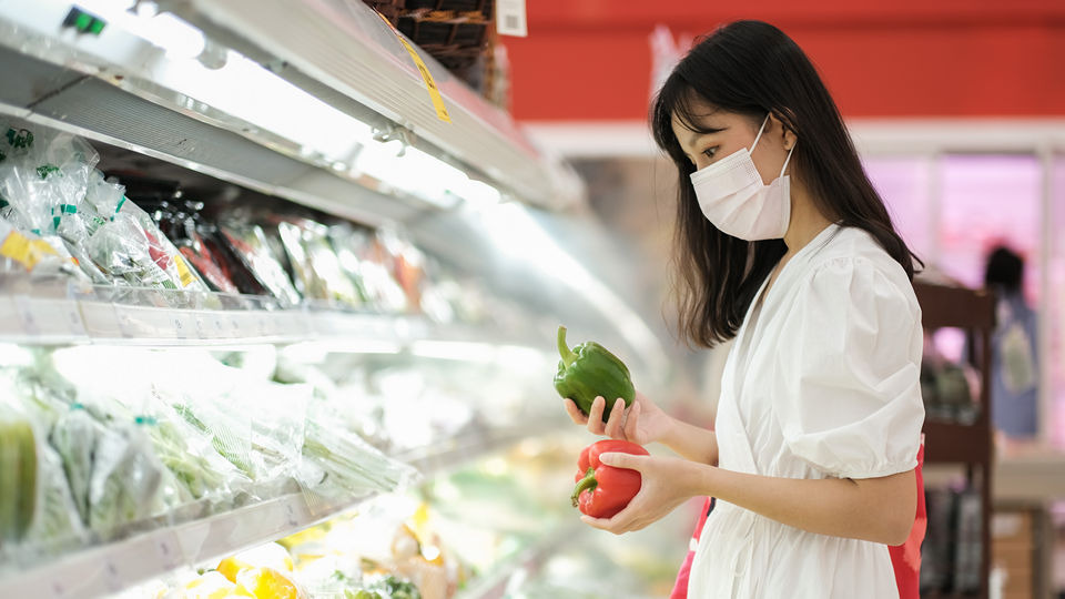 masked female shopper comparing produce in retail supermarket