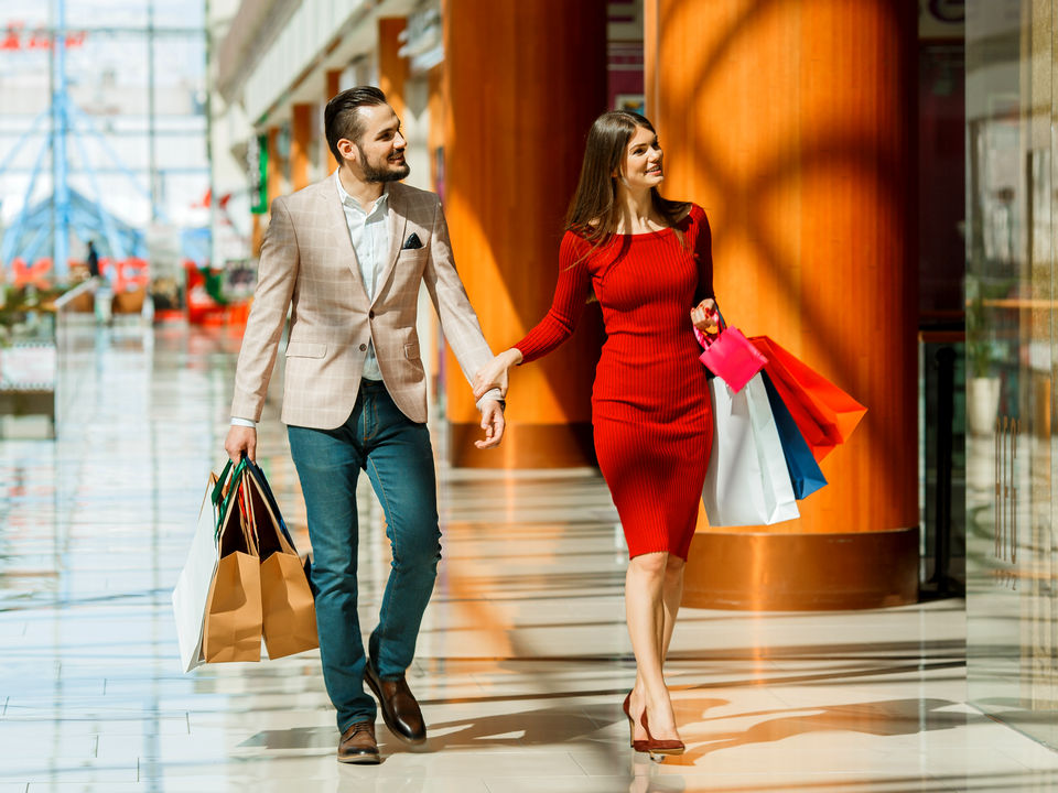 man and woman shoppers walking through retail shopping mall carrying many shopping bags and looking in store displays