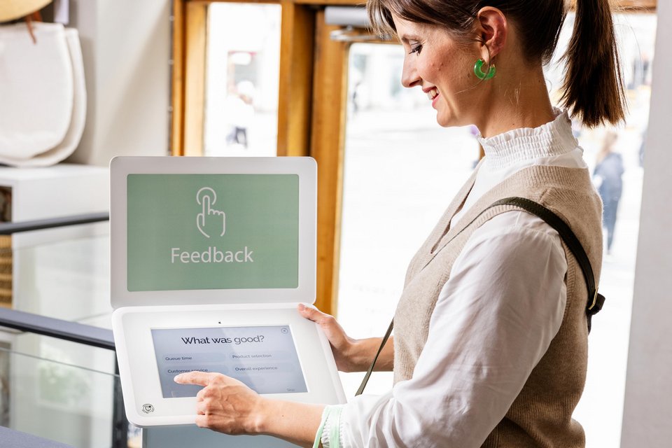 female shopper providing feedback at a happyornot kiosk tablet in a retail store