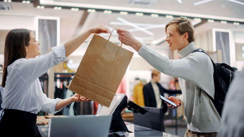 female retail sales associate handing shopping bag with purchased merchandise across the sales customer to male shopper