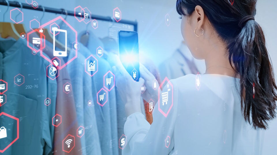 female shopper looks at rack of merchandise in retail apparel store through mobile phone with data and networking symbols superimposed