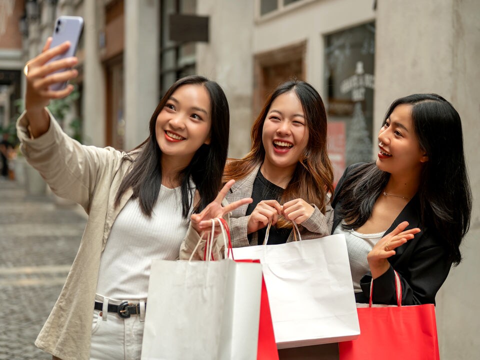 3 young female shoppers carrying shopping bags posing for a selfie outside a retail store
